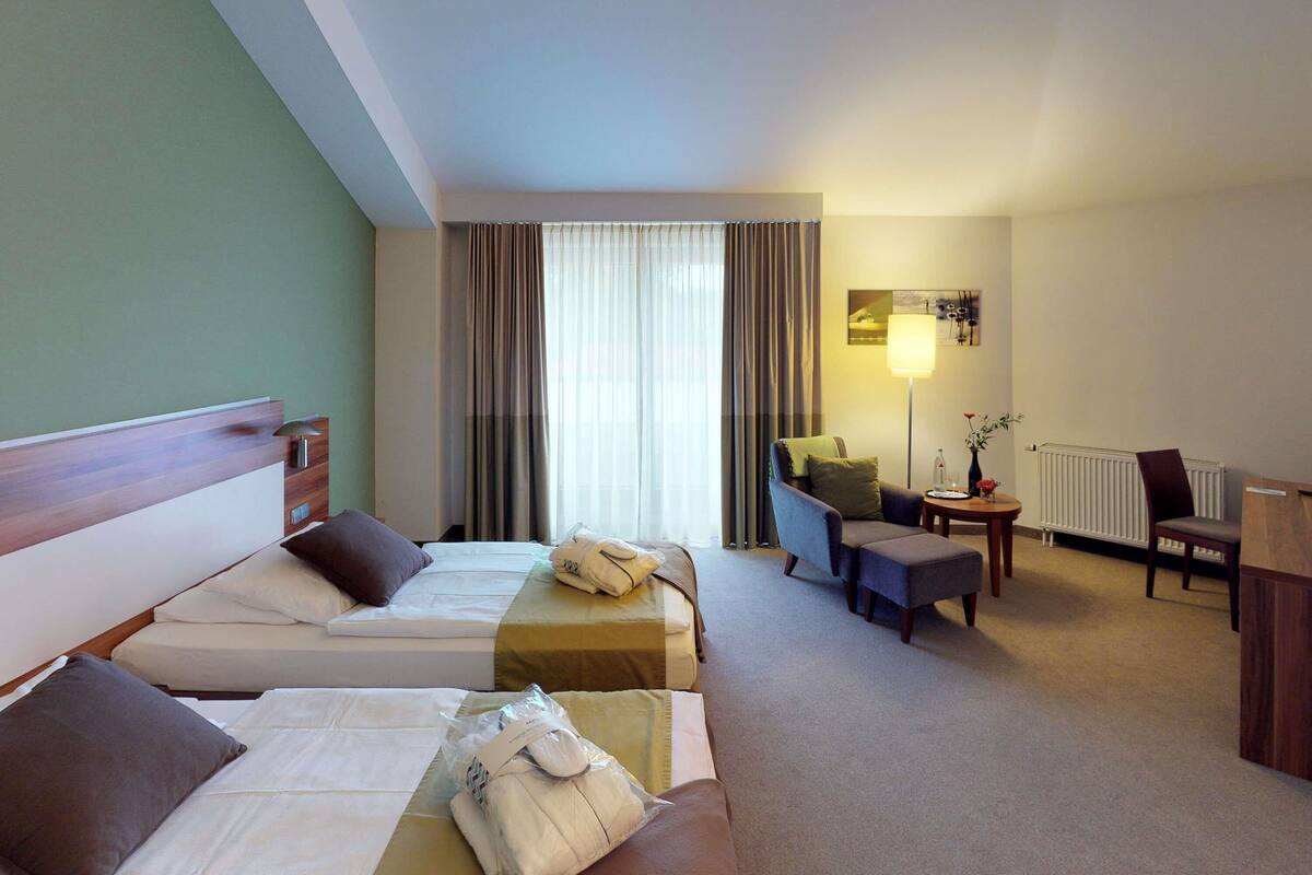 Habitación de hotel con dos camas, un escritorio, una silla, una lámpara y un radiador.