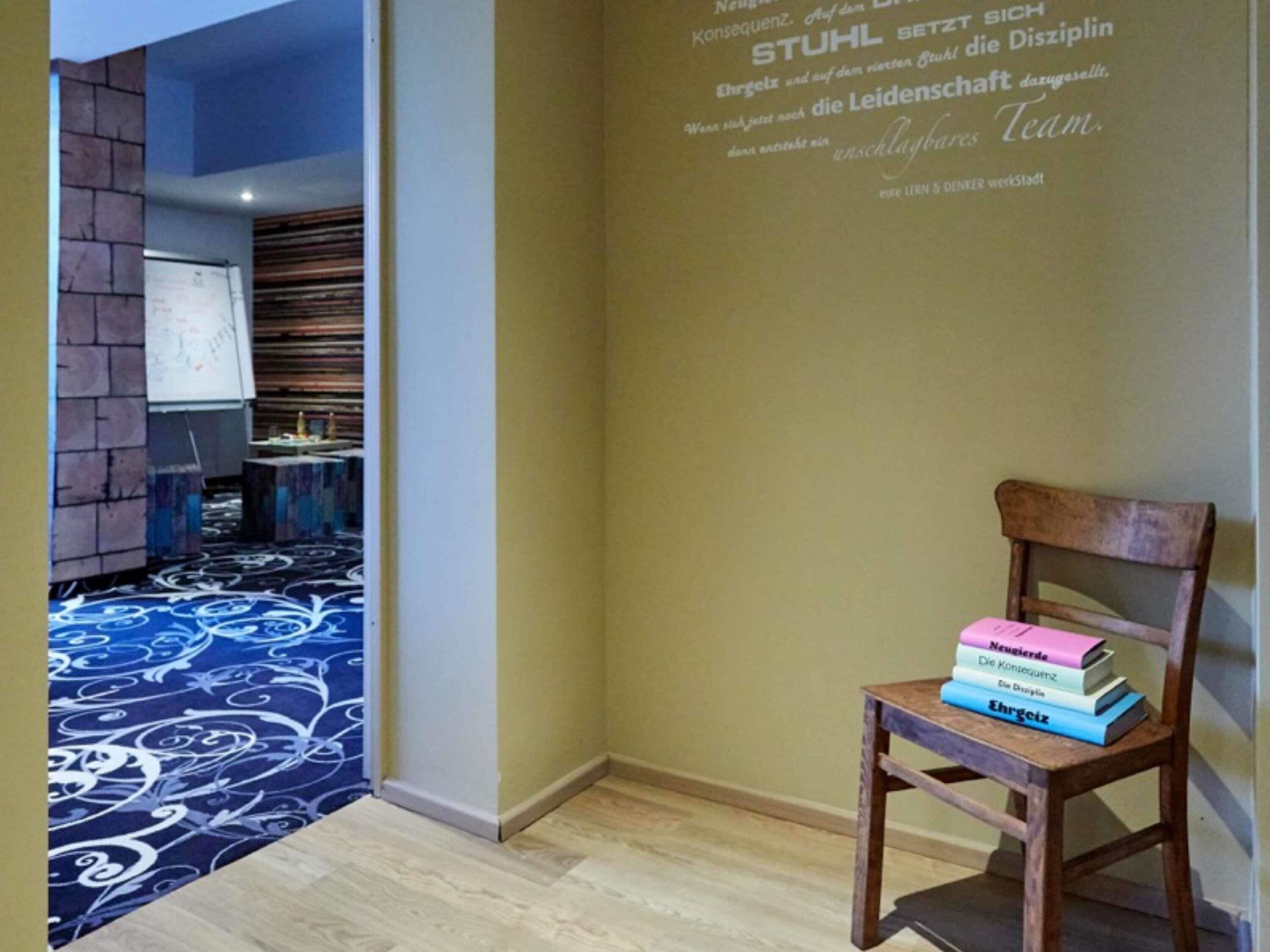 Una habitación con alfombra estampada, una silla de madera con libros y una pared con texto.