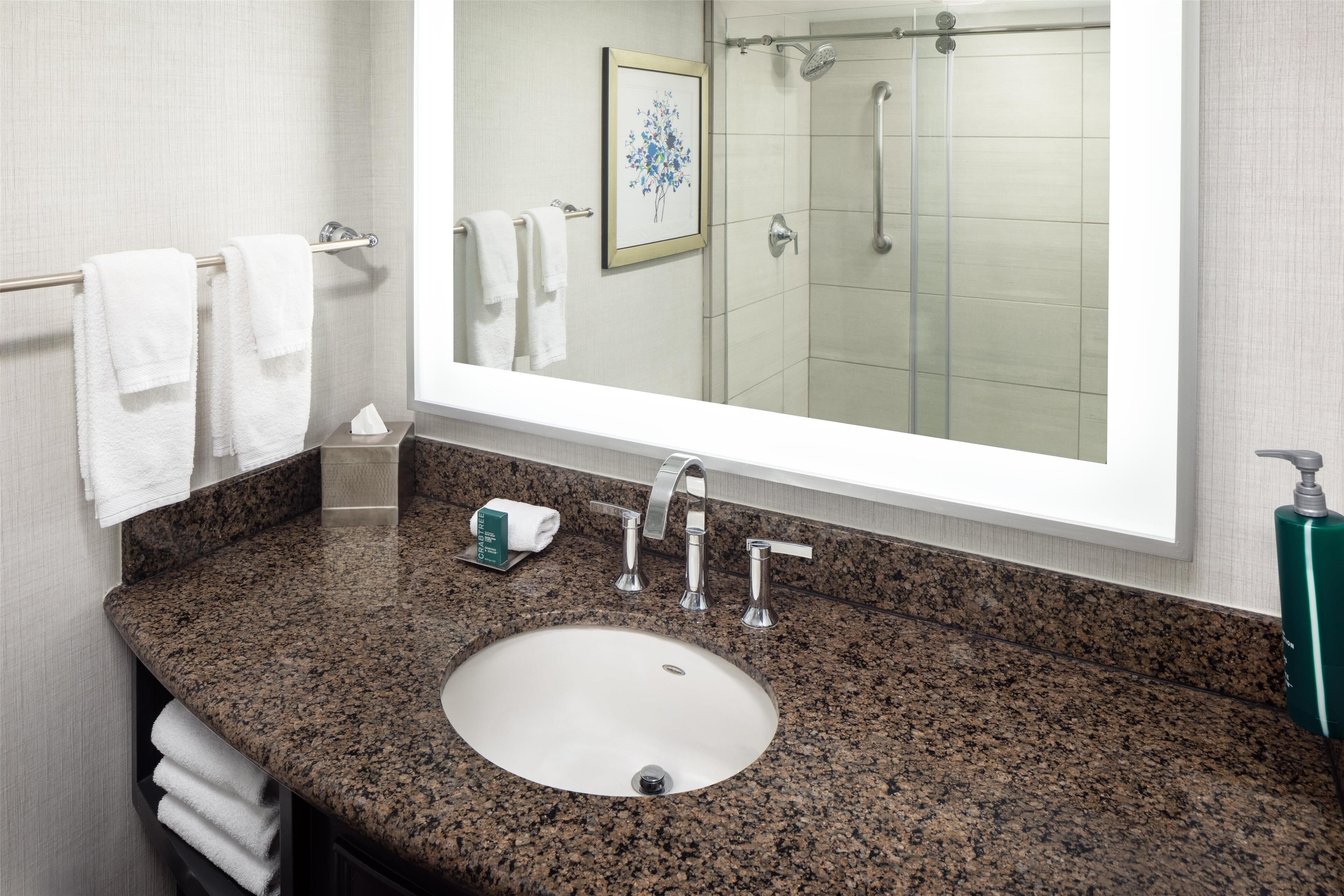 A bathroom with a granite countertop sink, a large mirror, and a glass shower enclosure.