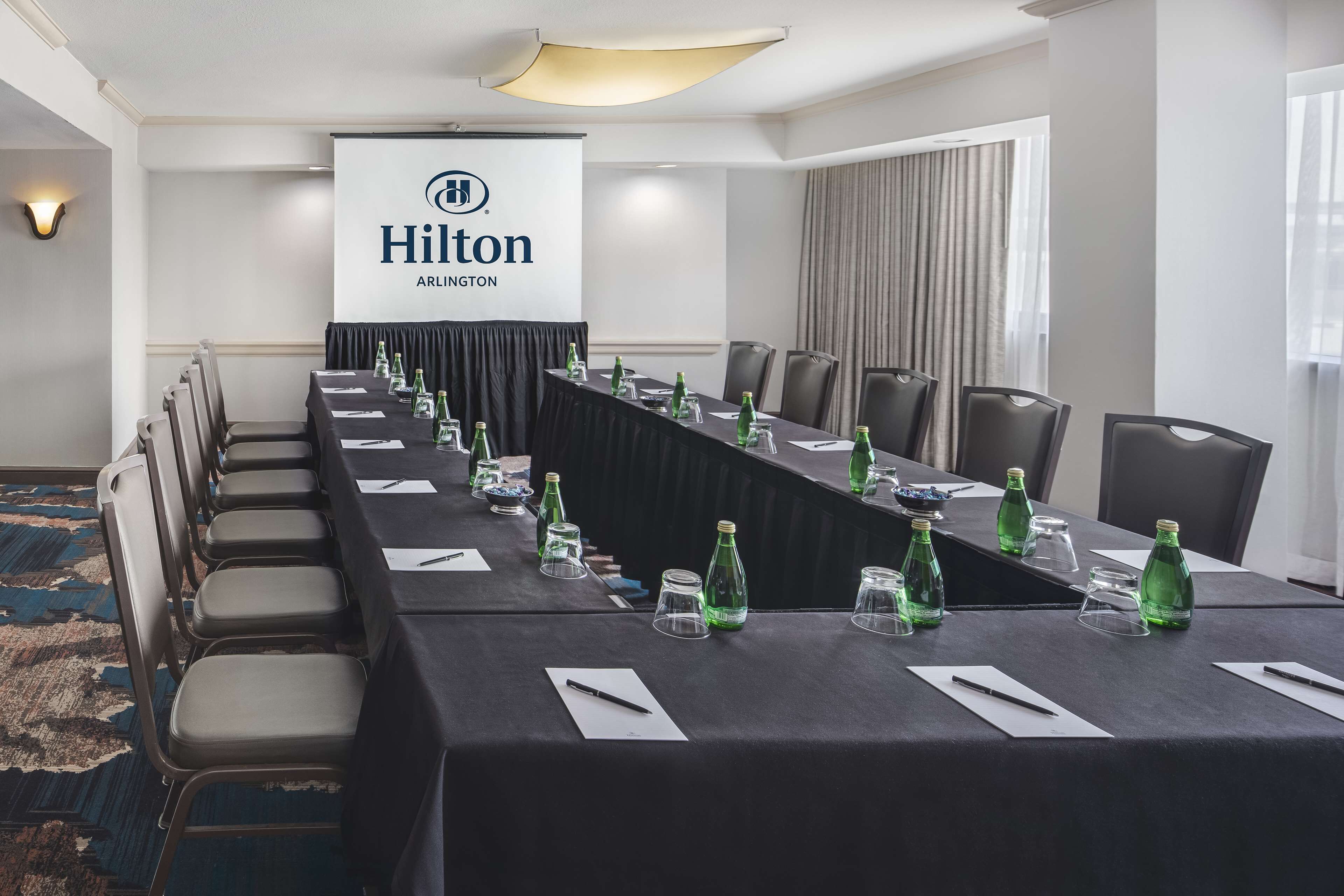 A conference room with a long table, chairs, and a projector screen displaying the Hilton logo.