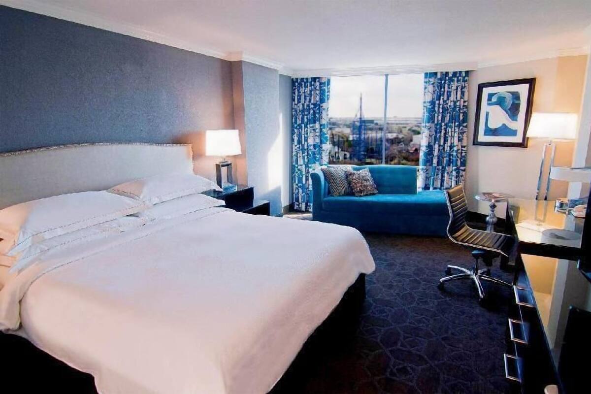 A hotel room with a large bed, a desk with a chair, a sofa, and a television.