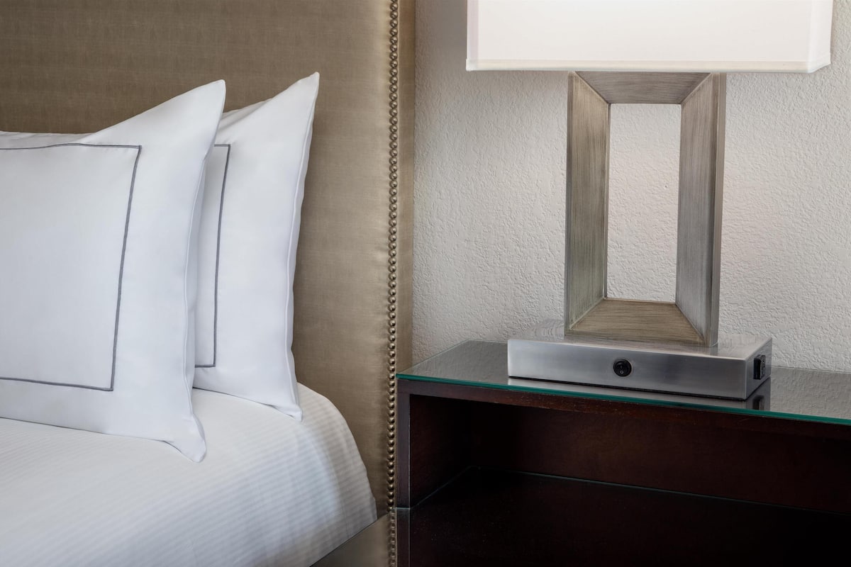A neatly made bed with white linens and pillows, a bedside table with a lamp, and a mirror.