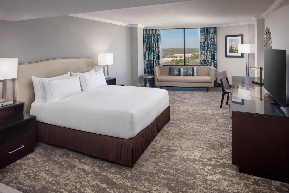 A hotel room with a large bed, a sofa, a TV, and a desk.