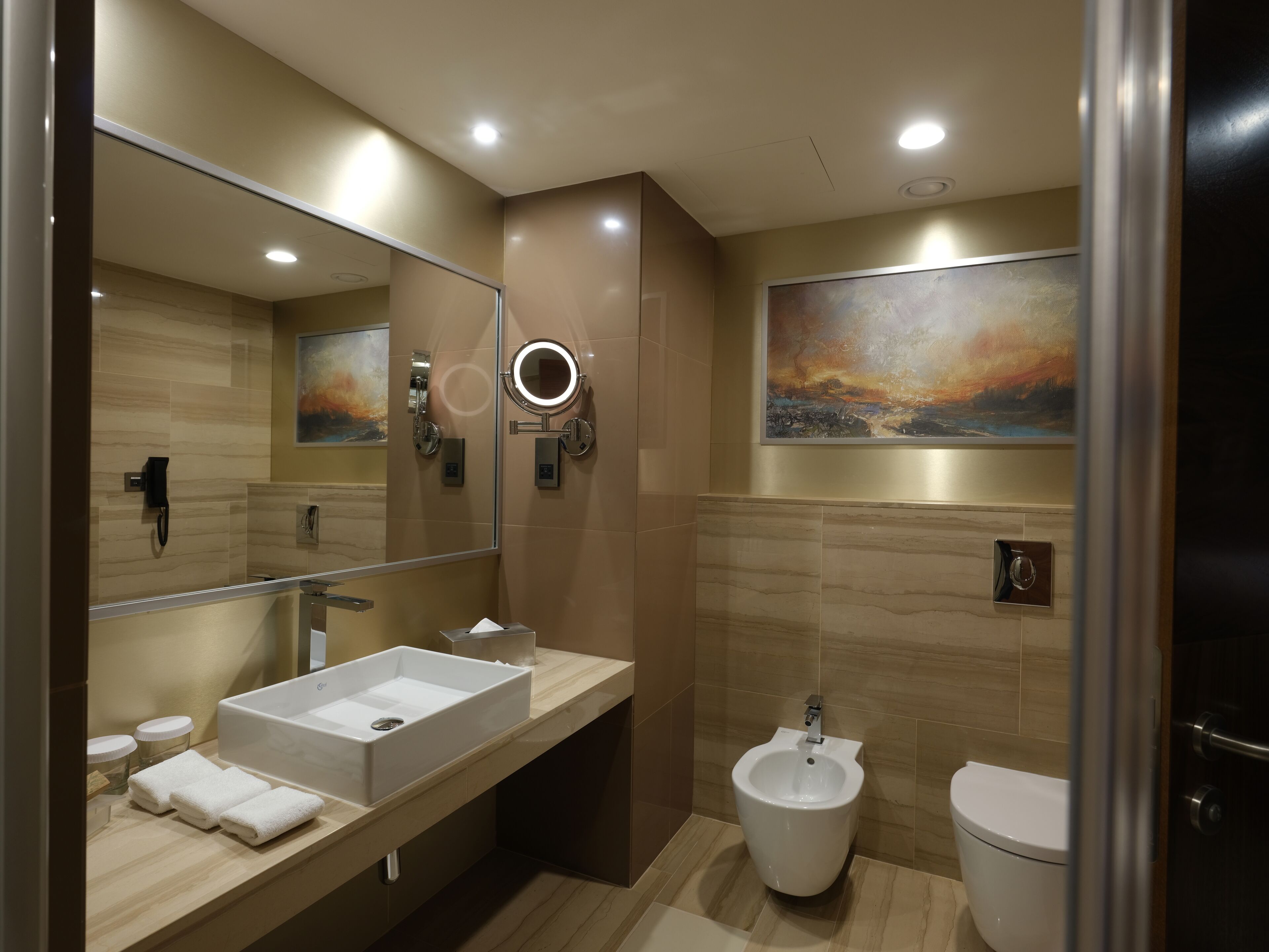 Un baño moderno con un espejo grande, un bidé, un inodoro y un mueble de tocador con lavamanos y dispensador de toallas.