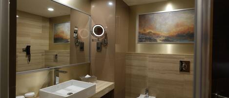 A modern bathroom with a large mirror, a bidet, a toilet, and a vanity with a sink and towel dispenser.