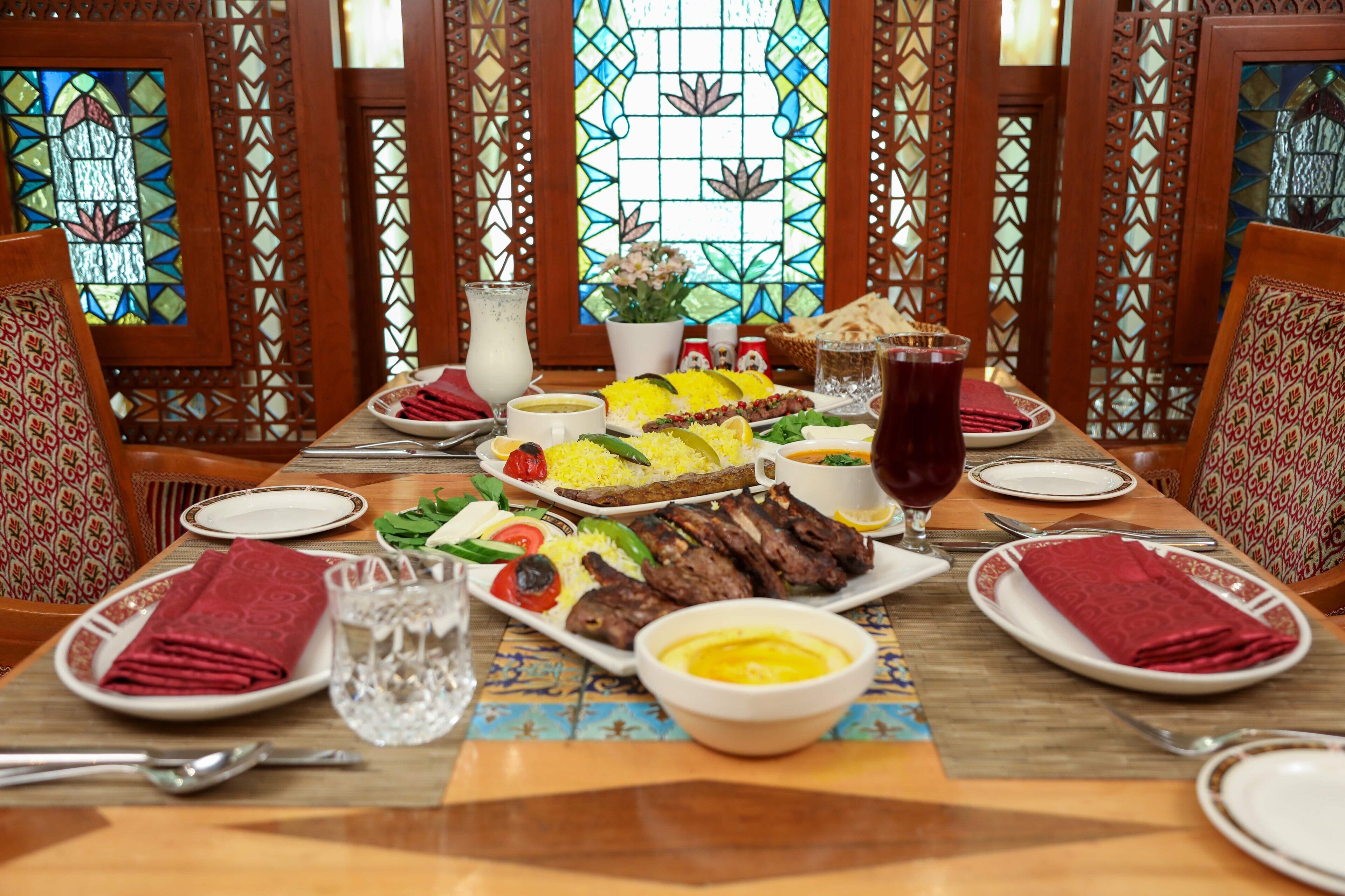 A dining table set with various dishes, including rice, meat, and vegetables, in a room with wooden lattice partitions and stained glass windows.