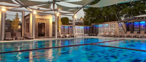 A swimming pool with lounge chairs and umbrellas, surrounded by a modern architectural design.