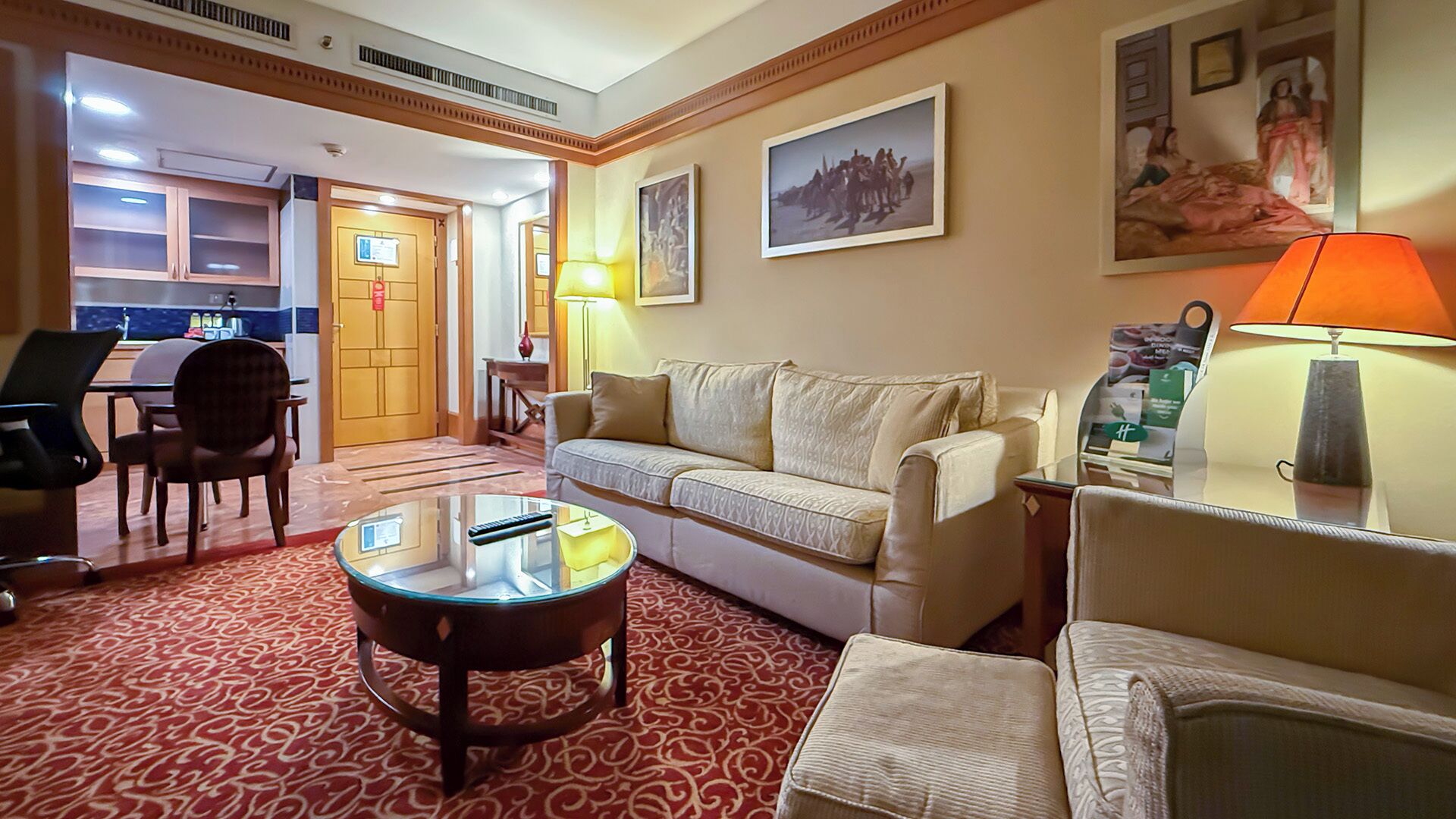 Een hotel lobby met een bank, fauteuils, een salontafel, een bureau en een eethoek.