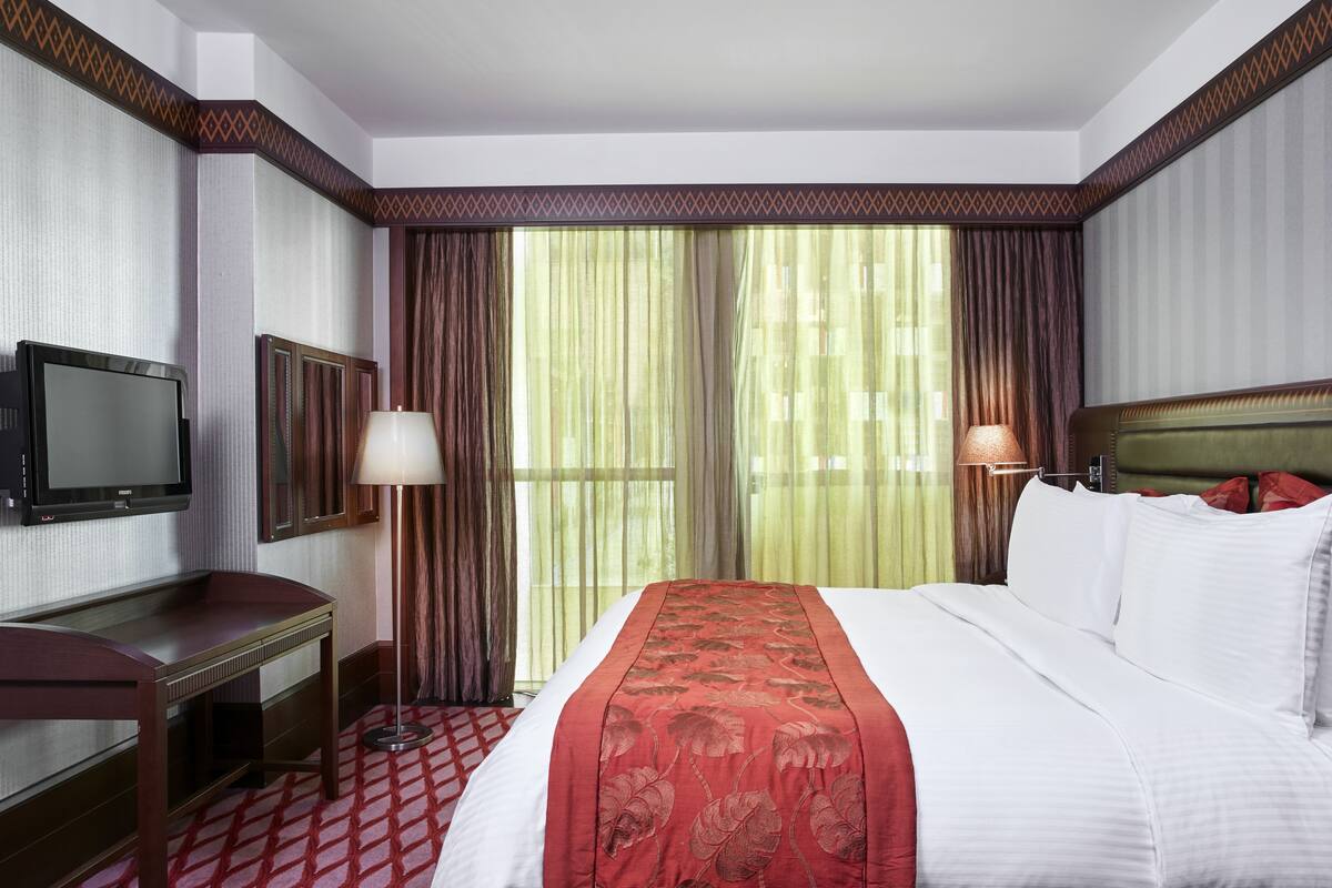 A hotel room with a large bed, a desk, a television, and a window with curtains.