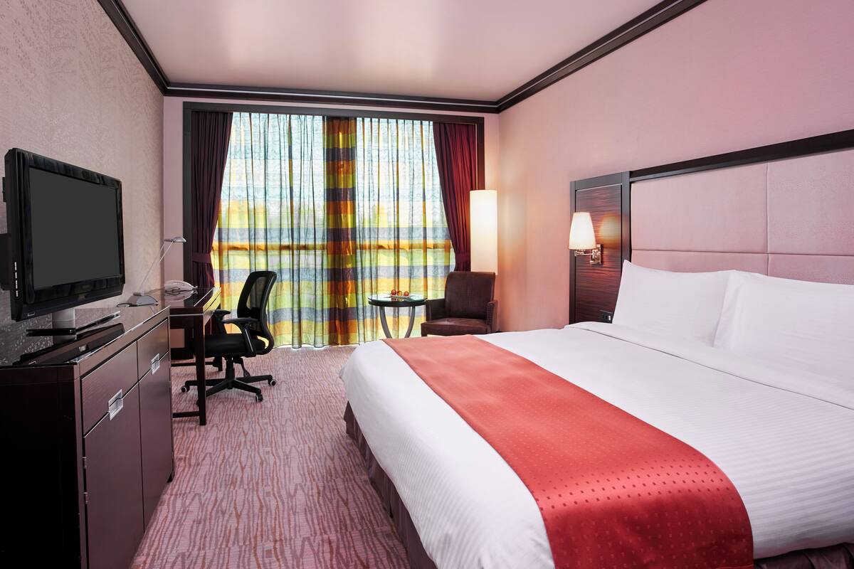 A hotel room with a bed, desk, chair, TV, and a window with curtains.