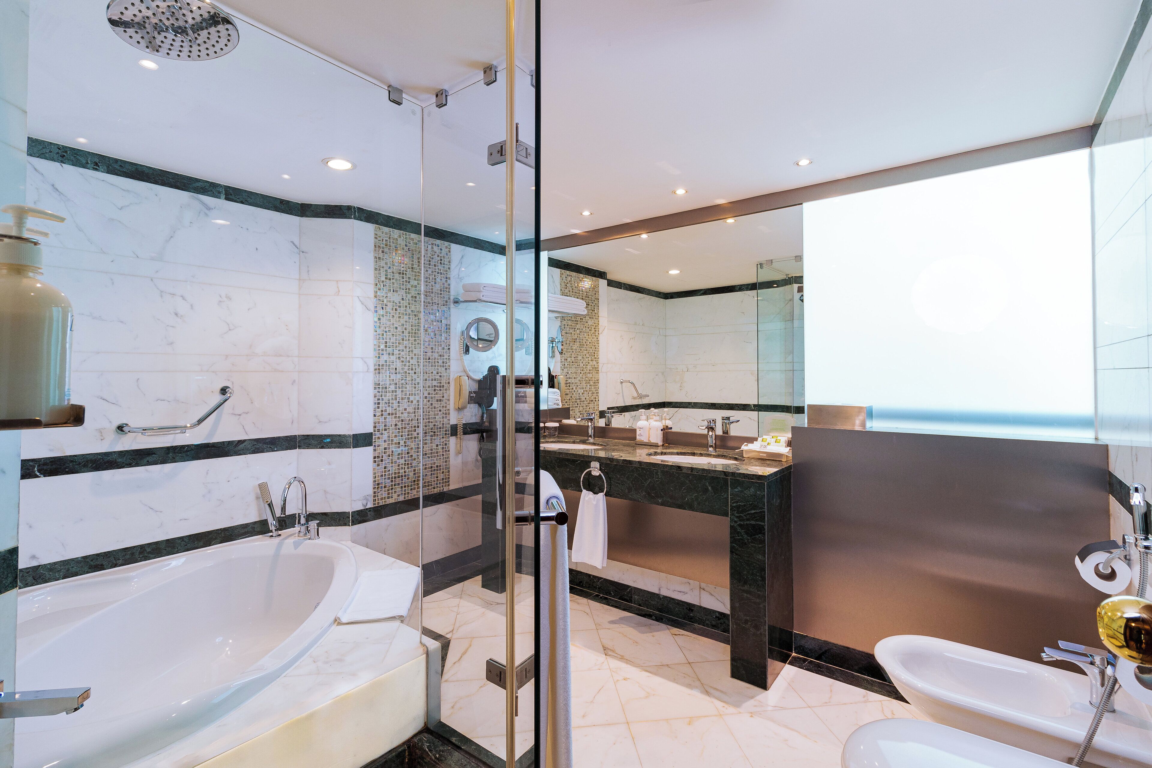 A modern bathroom with a glass-enclosed shower, a large bathtub, and a separate sink area.