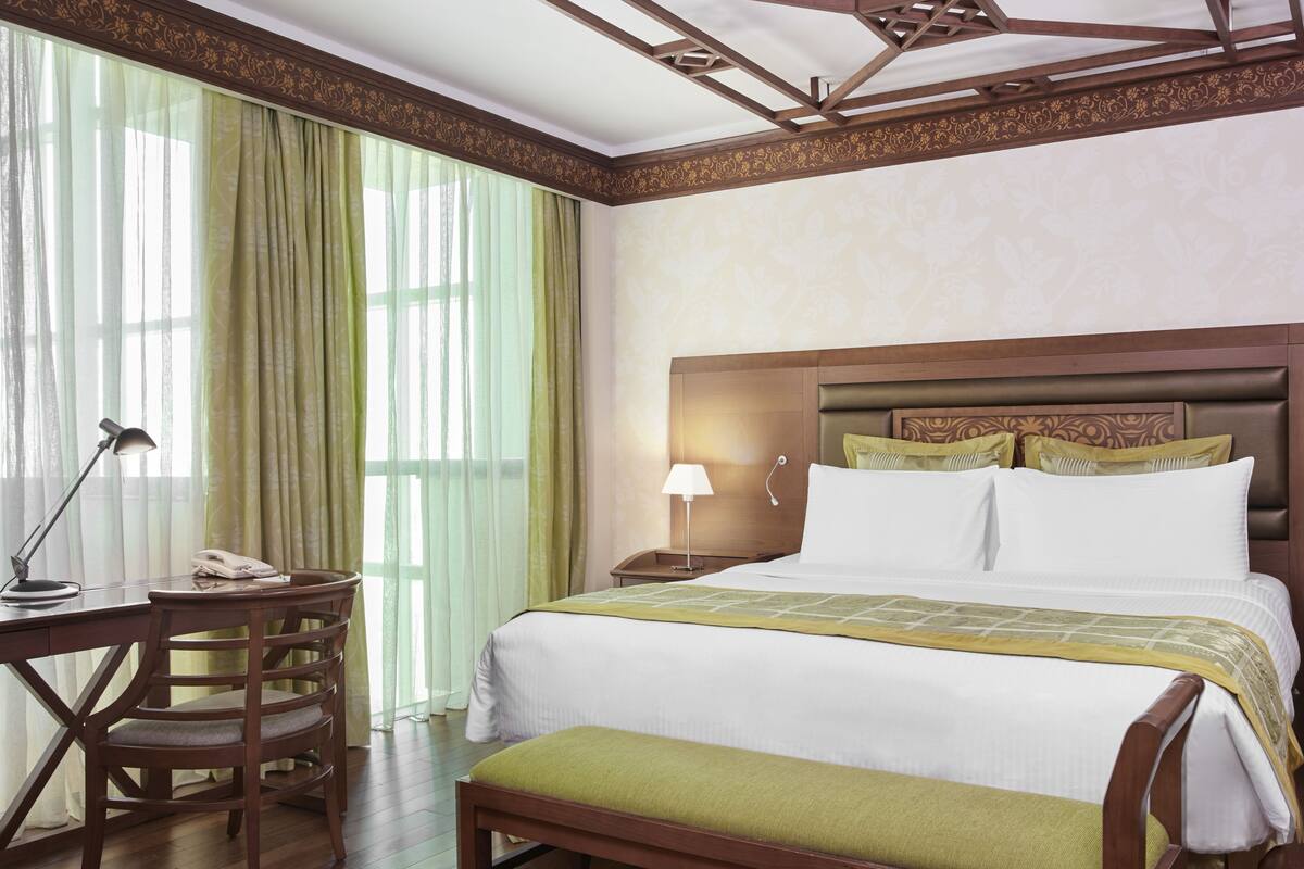 A hotel room with a bed, a desk, a chair, and a lamp.