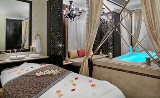 Habitación de hotel con una cama grande, una zona de estar separada, una bañera y un espejo amplio.
