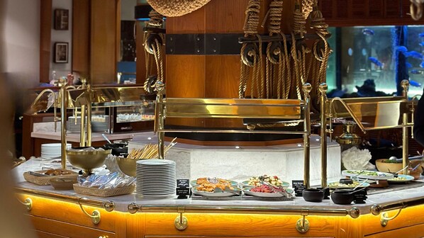 A buffet setup with various dishes, a central serving station, and a decorative rope structure. - Holiday Inn Kuwait Al Thuraya City by IHG (Farwaniya)