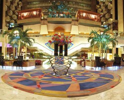 Un vestíbulo de hotel con una pieza decorativa central, varias zonas de estar y una escalera que conduce a plantas superiores.