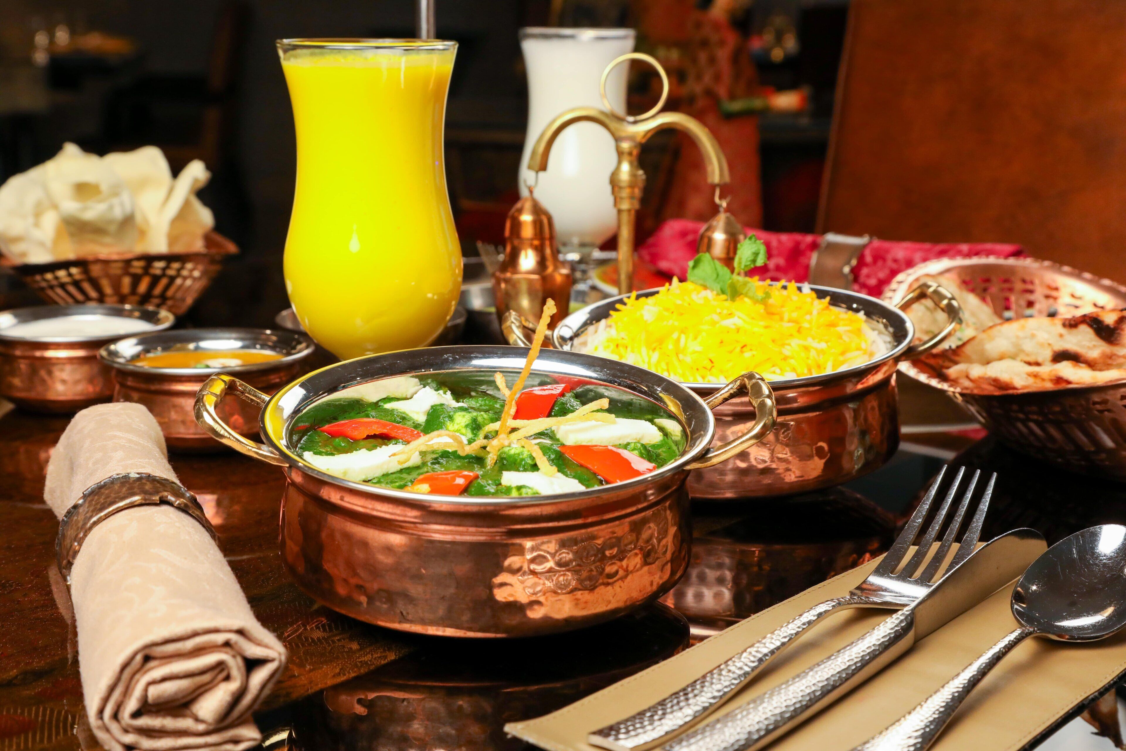 A table set with traditional Indian cuisine, including a copper dish of mixed vegetables, a bowl of rice, and a glass of orange juice.