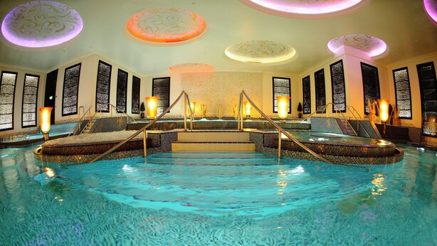 An indoor swimming pool with steps leading to a central area, surrounded by seating and decorative lighting. - Holiday Inn Kuwait Al Thuraya City by IHG (Farwaniya)