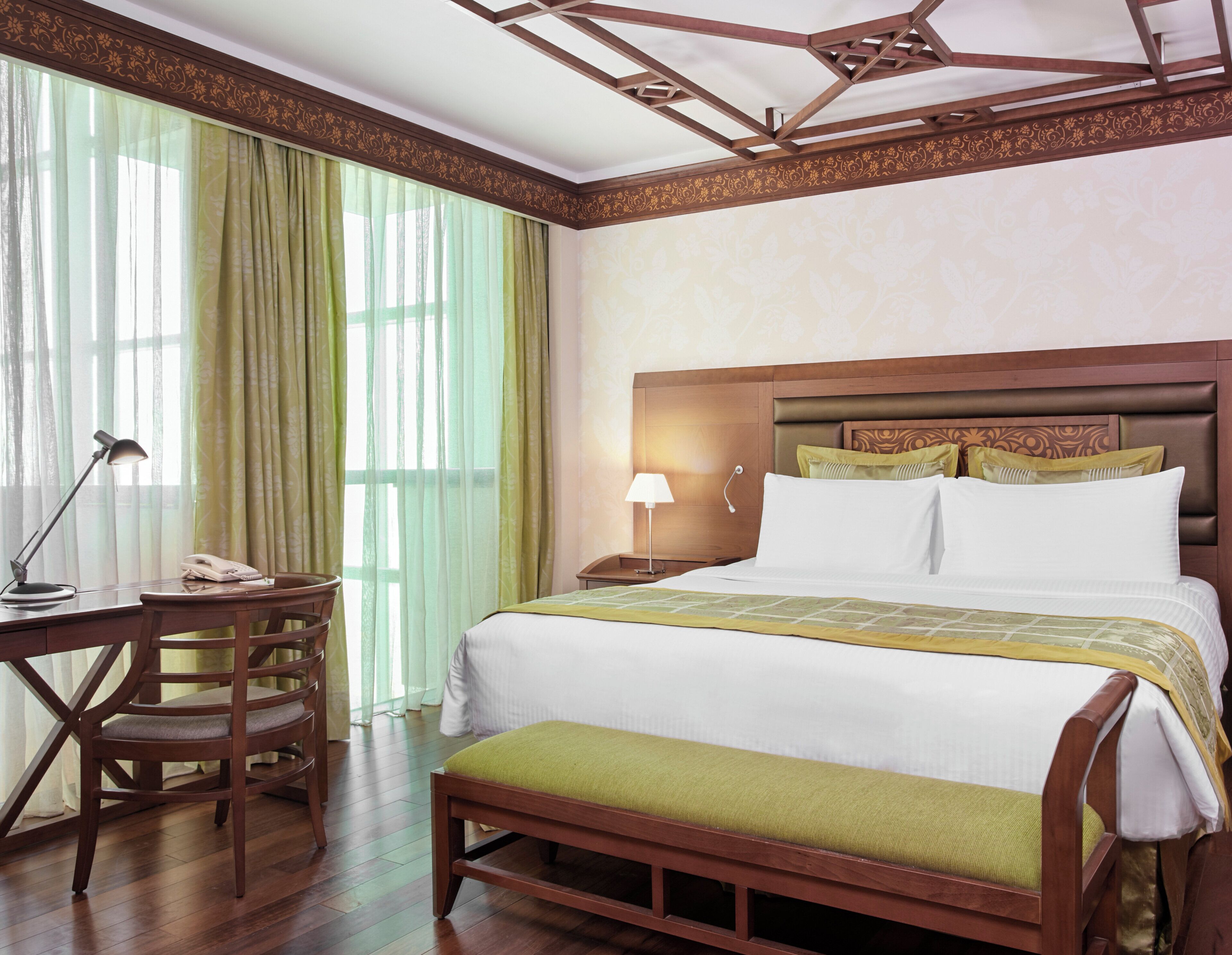 A hotel room with a wooden bed, a desk with a lamp, and a chair.