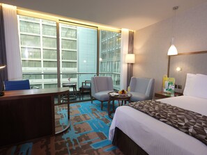 A hotel room with a bed, two armchairs, a desk, a small table with a bowl of fruit, and a window with curtains. - Holiday Inn Kuwait Al Thuraya City by IHG (Farwaniya)