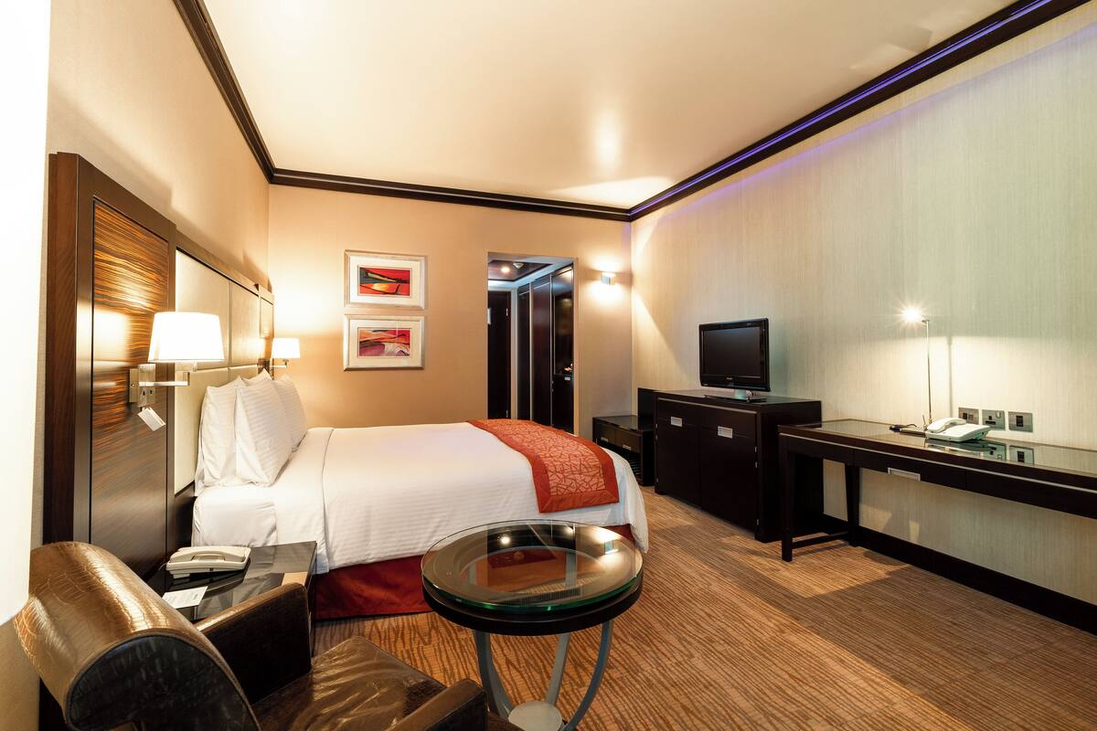 A hotel room with a bed, bedside table, lamp, desk, and television.