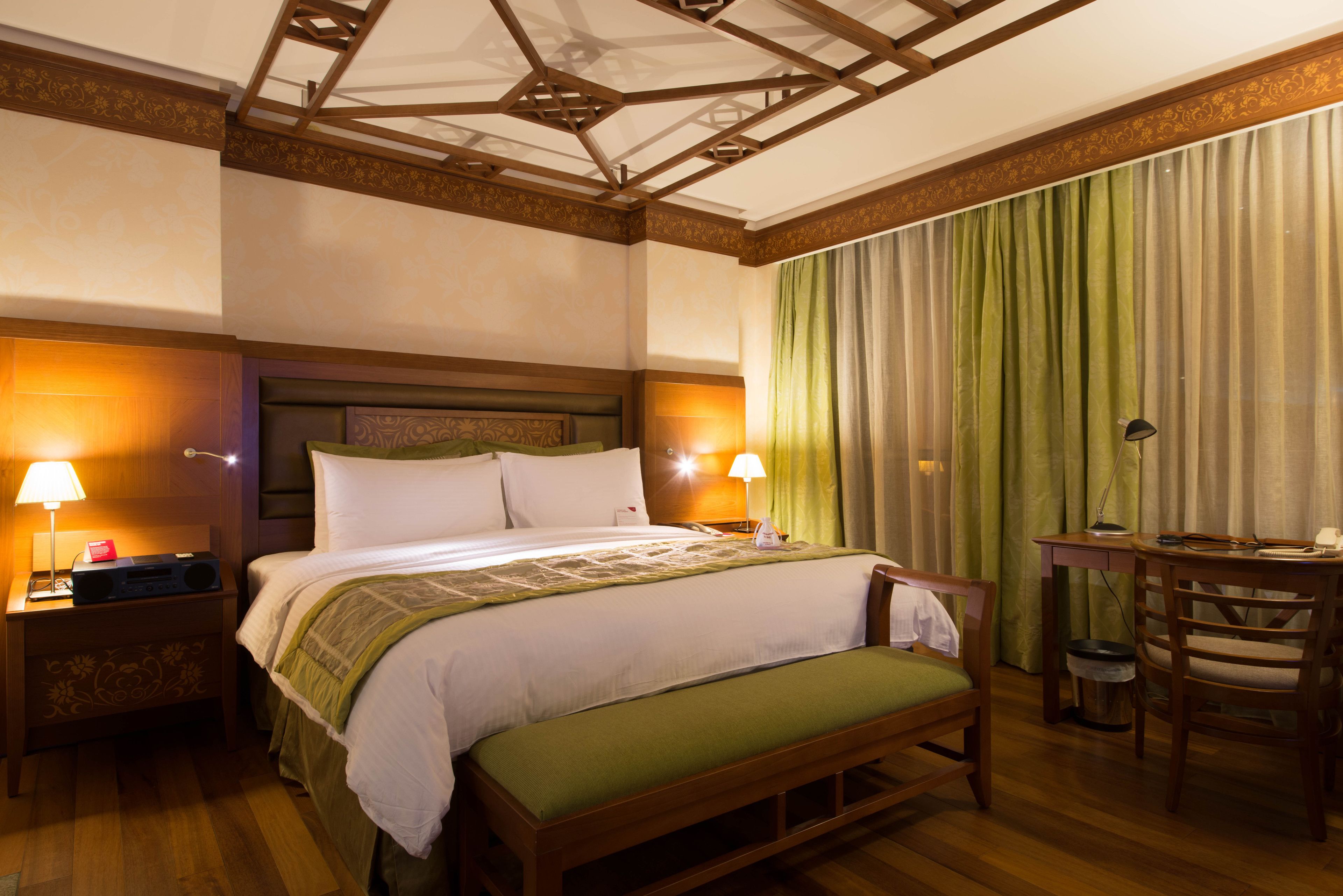 Een hotelkamer met een groot bed, nachtlampjes, een houten bankje, een bureau en een stoel.