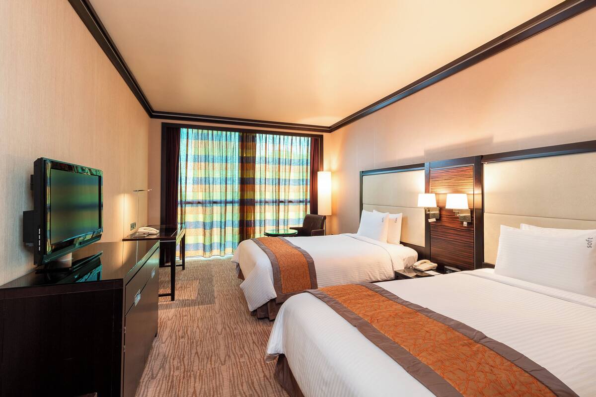 A hotel room with two beds, a television, a desk, and a window with curtains.