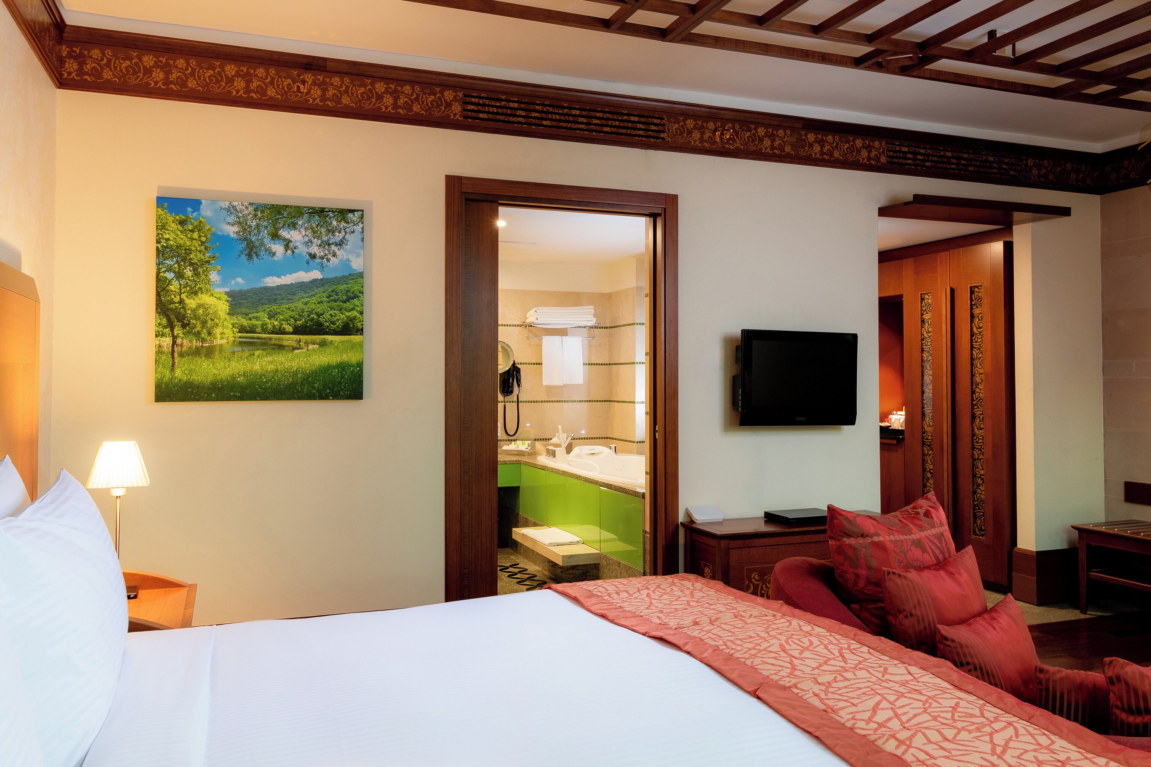 A hotel room with a bed, a desk, a chair, a TV, and a bathroom visible through an open door.