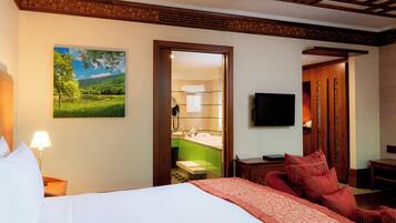 A hotel room with a bed, a desk, a chair, a TV, and a bathroom visible through an open door.