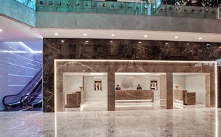A hotel lobby with a reception desk, marble flooring, and a glass railing overlooking a lower level.