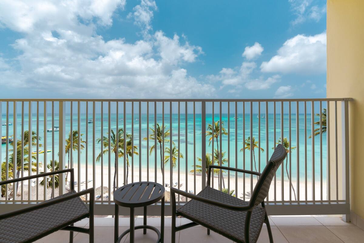 A balcony with a view of a beach, palm trees, and the ocean.