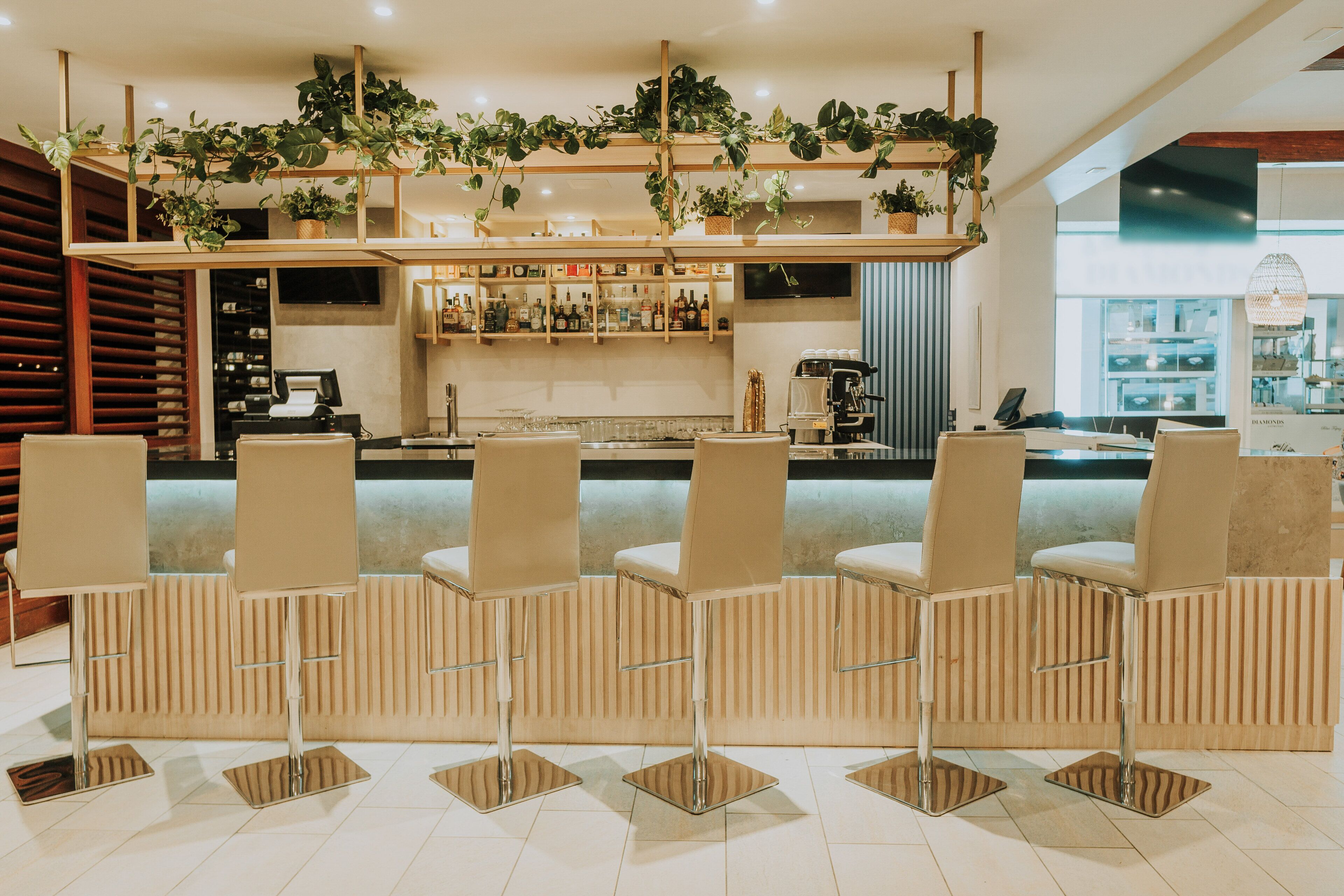 Una zona de bar con mostrador, taburetes y estanterías llenas de botellas.
