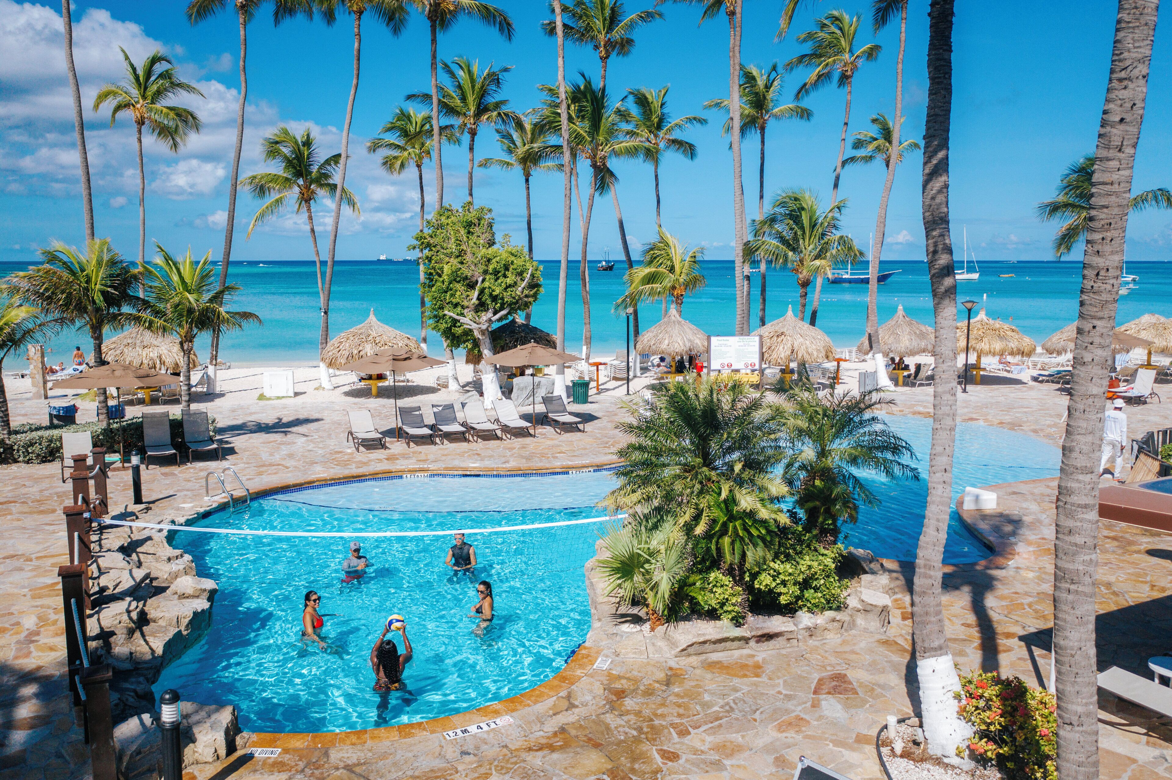 A pool area with a clear view of the ocean, surrounded by palm trees and lounge chairs.