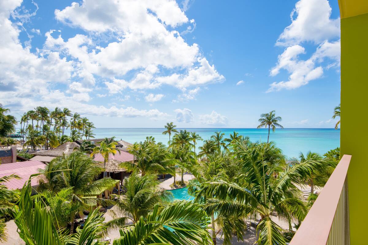 A resort with a pool surrounded by palm trees and a view of the ocean.