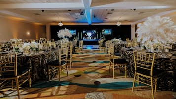A banquet hall with round tables, gold chairs, and a stage with screens.
