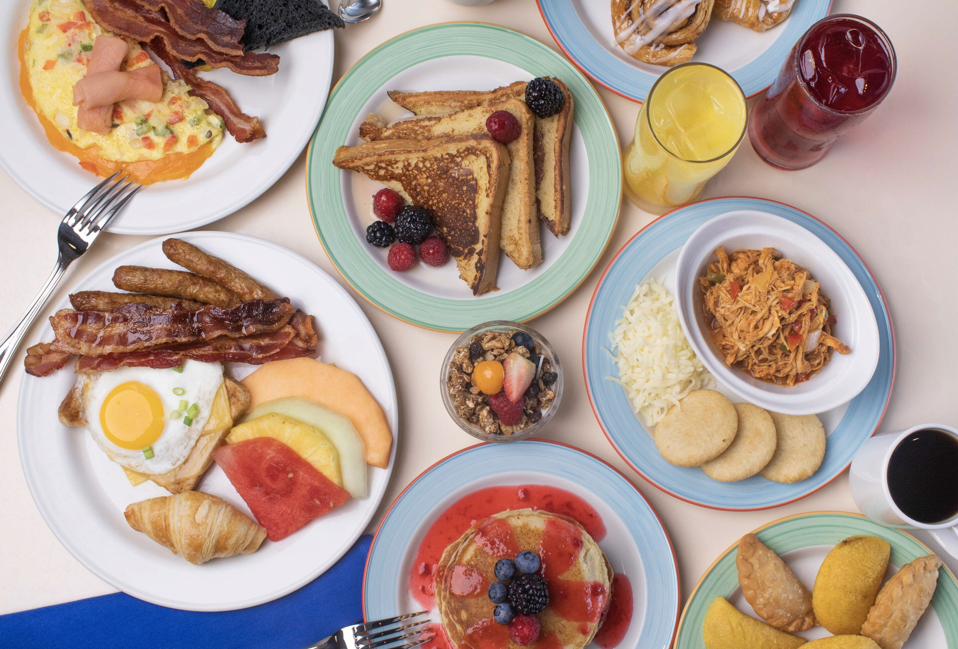 Una mesa con una variedad de platos para el desayuno, incluyendo tostadas, huevos, tocino y frutas.