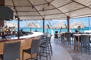 An outdoor bar area with a view of the ocean, thatched umbrellas, and wicker furniture.