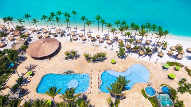 An aerial view of a beach resort with multiple swimming pools, palm trees, and thatched-roof huts. - Holiday Inn Resort Aruba - Beach Resort & Casino by IHG (Noord)