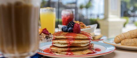 A breakfast setting with pancakes, berries, and croissants on a table.