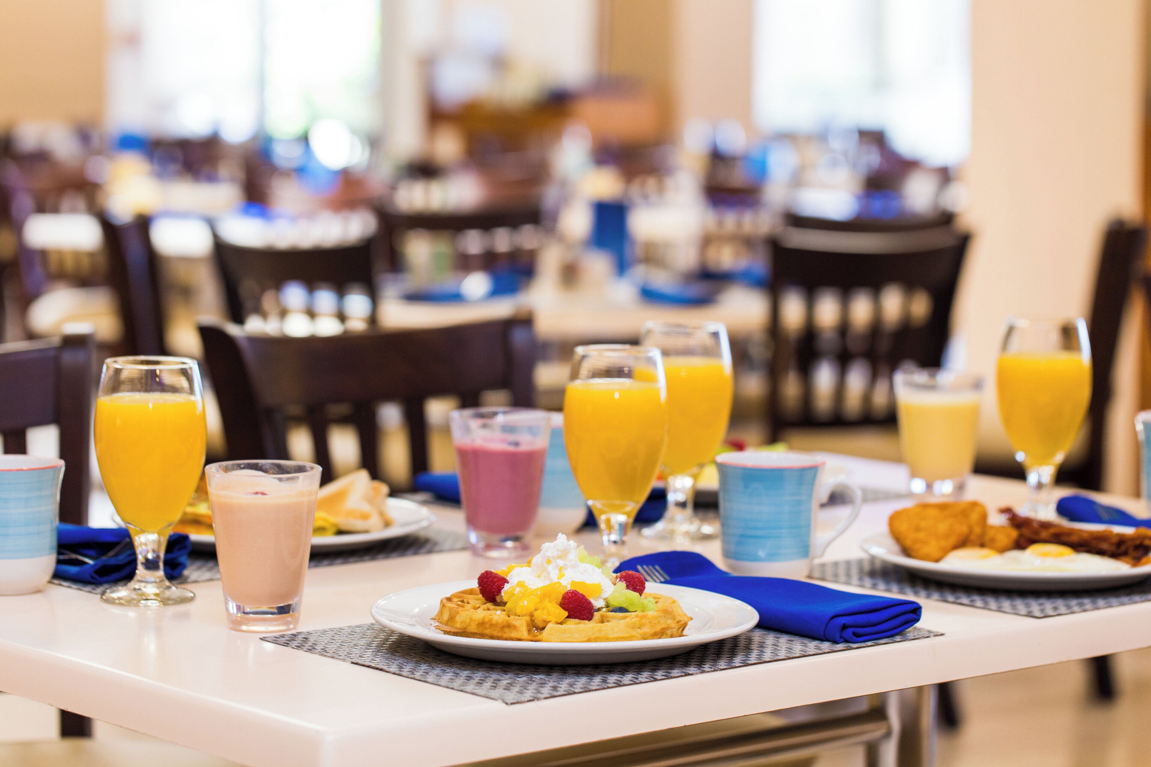 A breakfast setting with plates of food, glasses of orange juice, and a waffle topped with fruit.