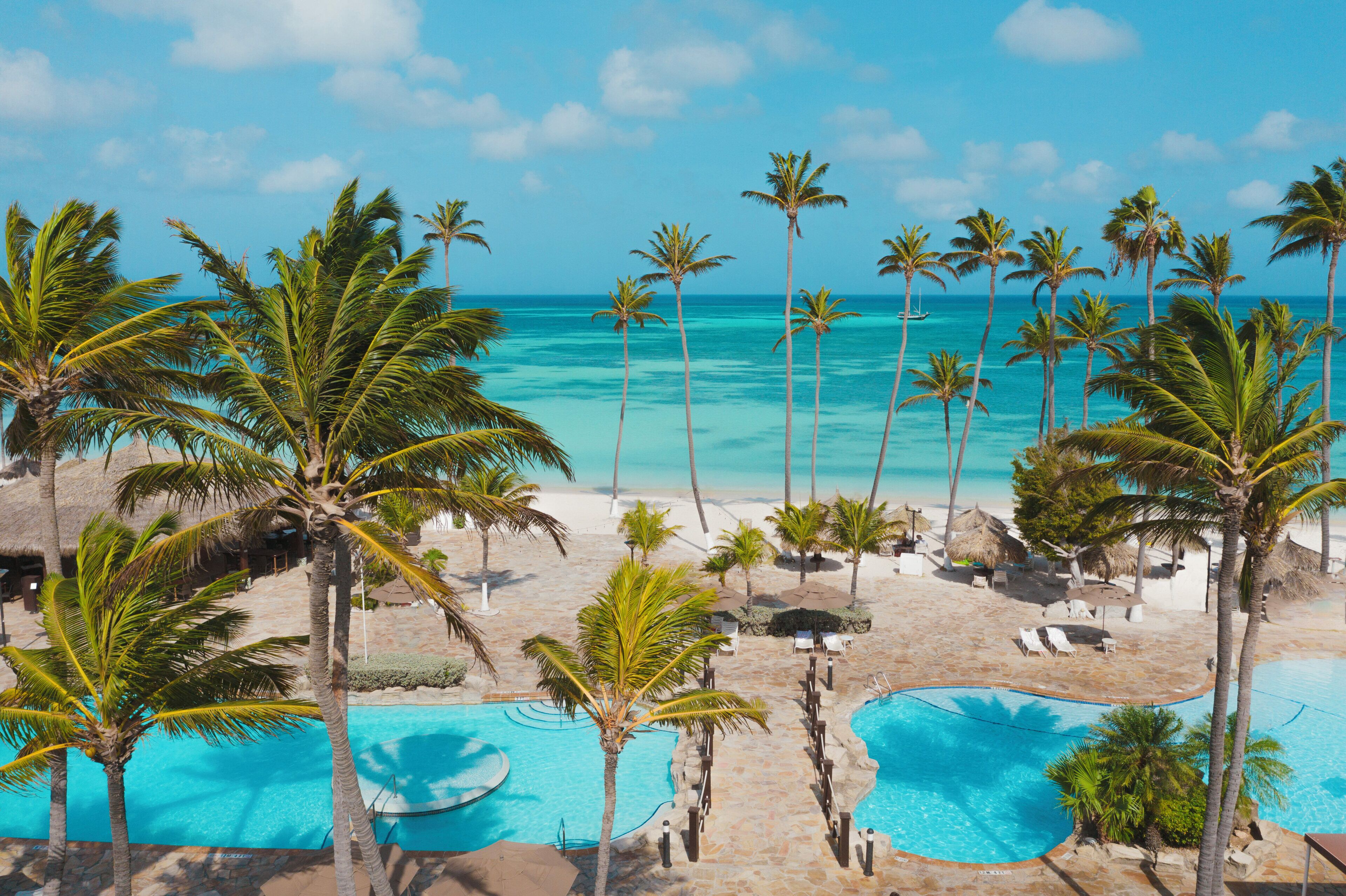 A resort with a pool area, palm trees, and a view of the ocean.