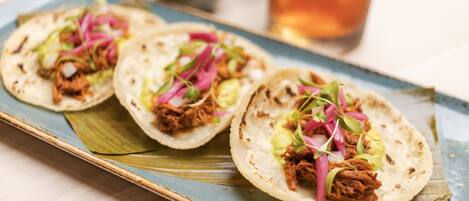 Three tacos on a blue plate with a drink in the background.