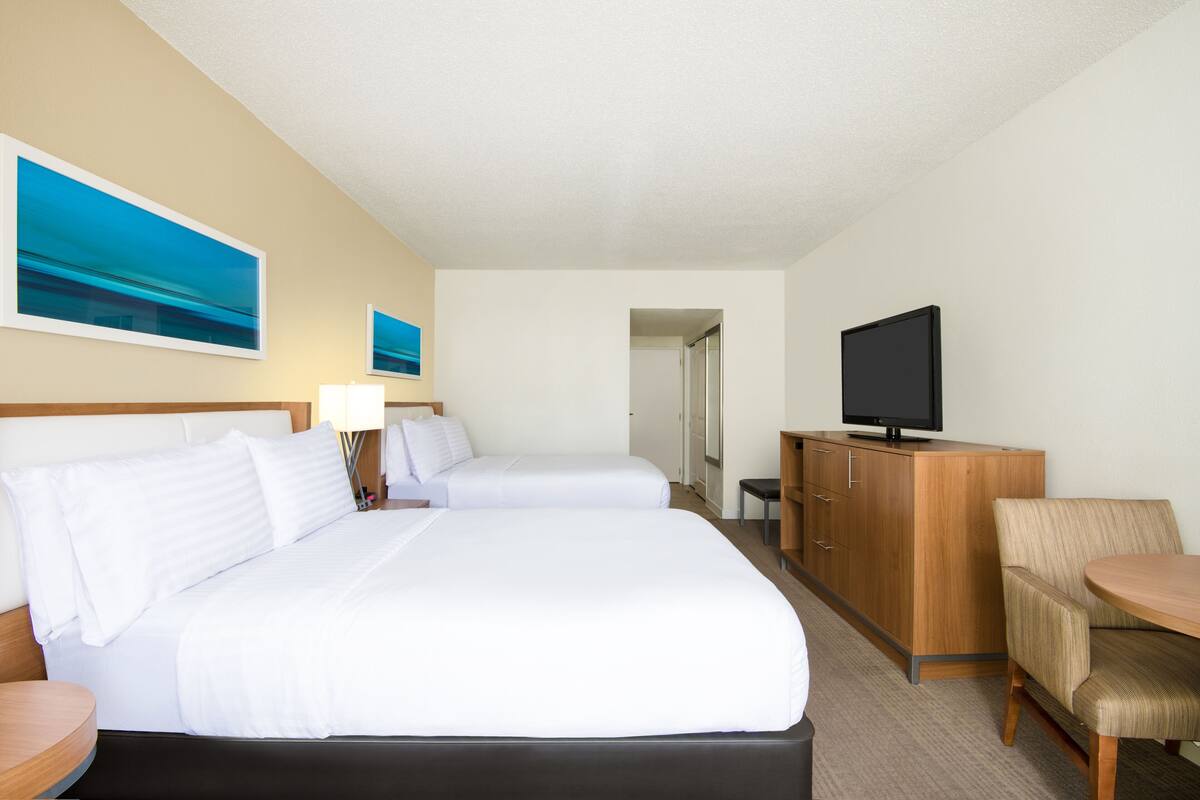 A hotel room with two beds, a television, a desk, and a chair.