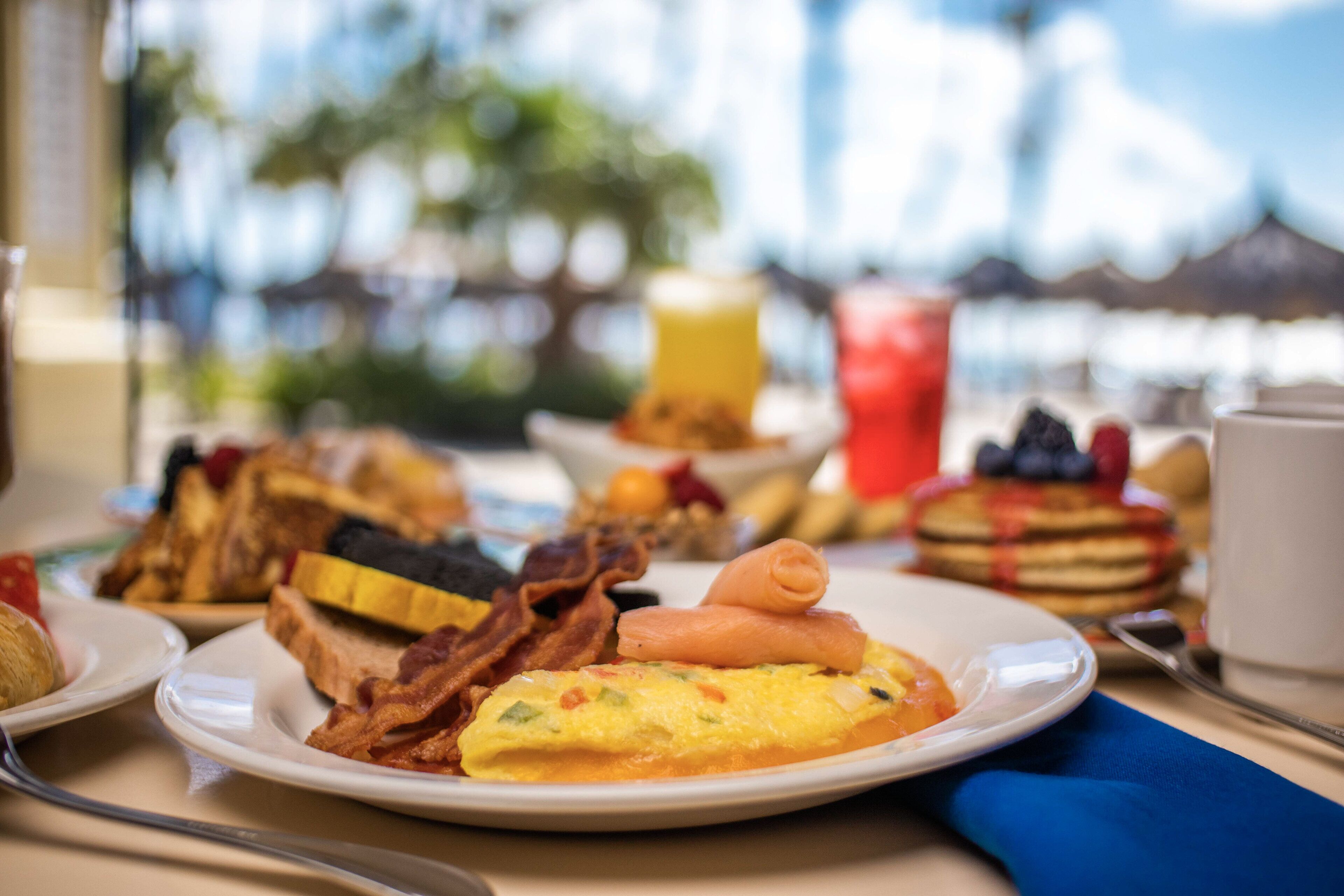Un assortiment de mets pour le petit-déjeuner, comprenant des toasts, du bacon, des œufs et des crêpes, disposés sur une table.