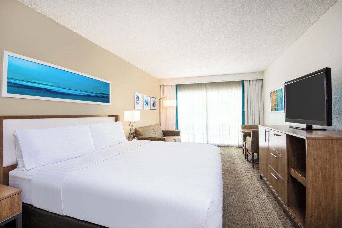 Habitación de hotel con una cama grande, televisión, escritorio con silla y ventana con cortinas.
