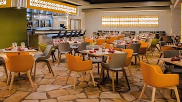 Un restaurante con varias mesas y sillas, una zona de bar y decoraciones de pared con diseños.