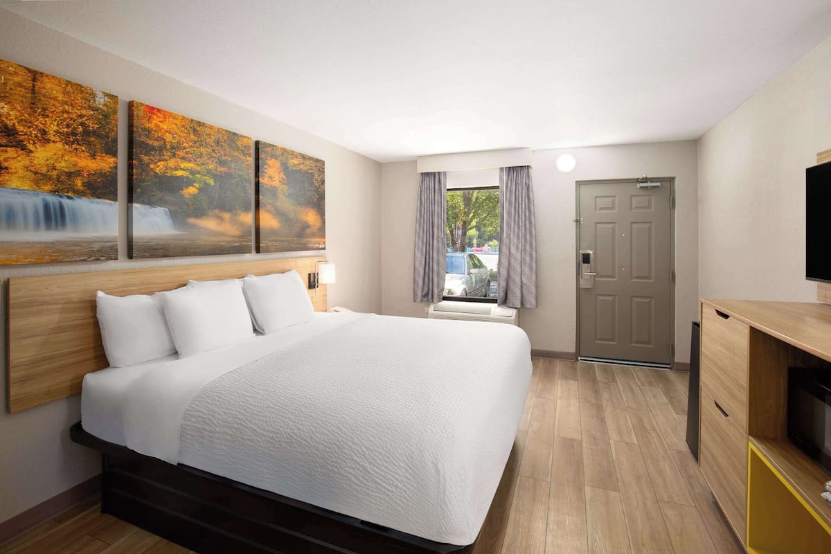 Quarto de hotel com uma cama grande, televisão, escrivaninha e janela com cortinas.