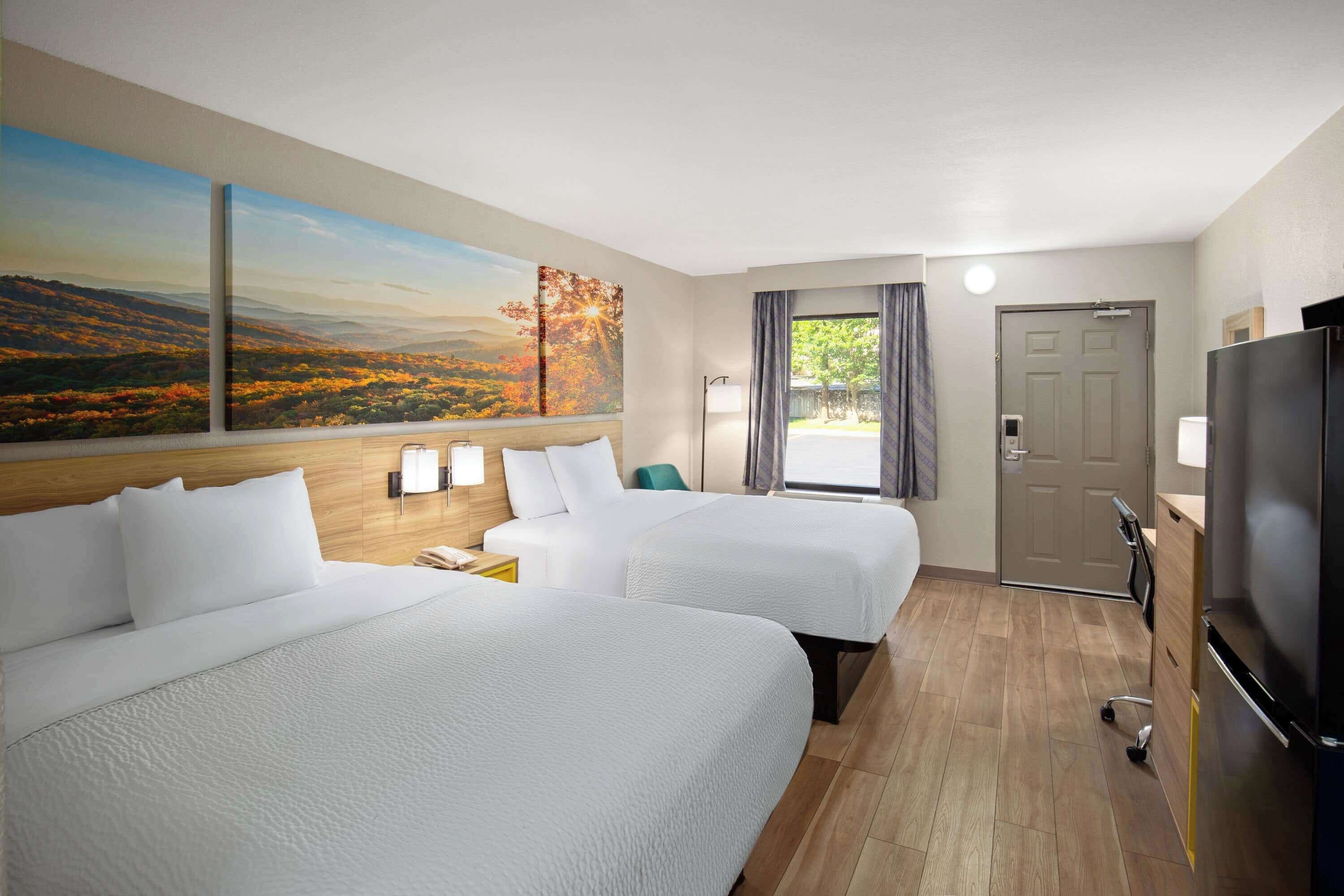 A hotel room with two beds, a TV, a desk, and a window with curtains.