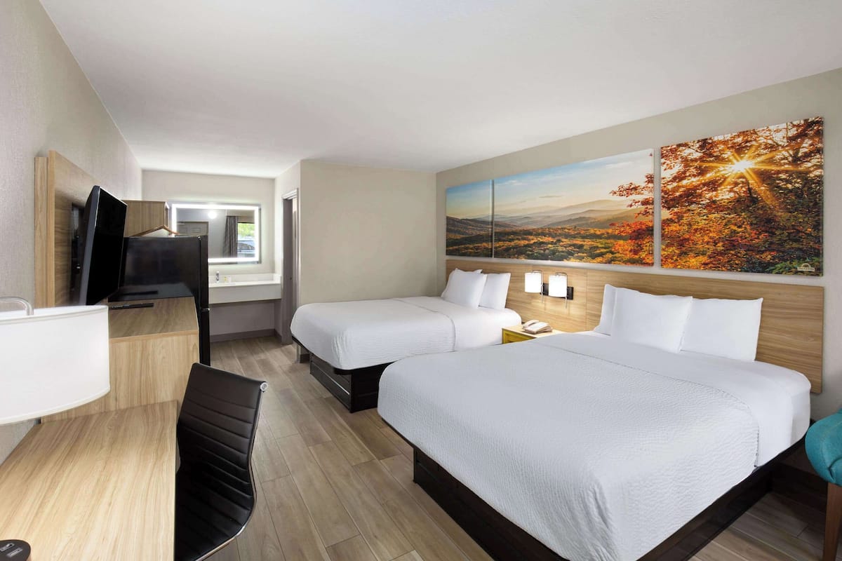 Quarto de hotel com duas camas, uma mesa de escritório, televisão e uma janela ampla com vista para a paisagem.