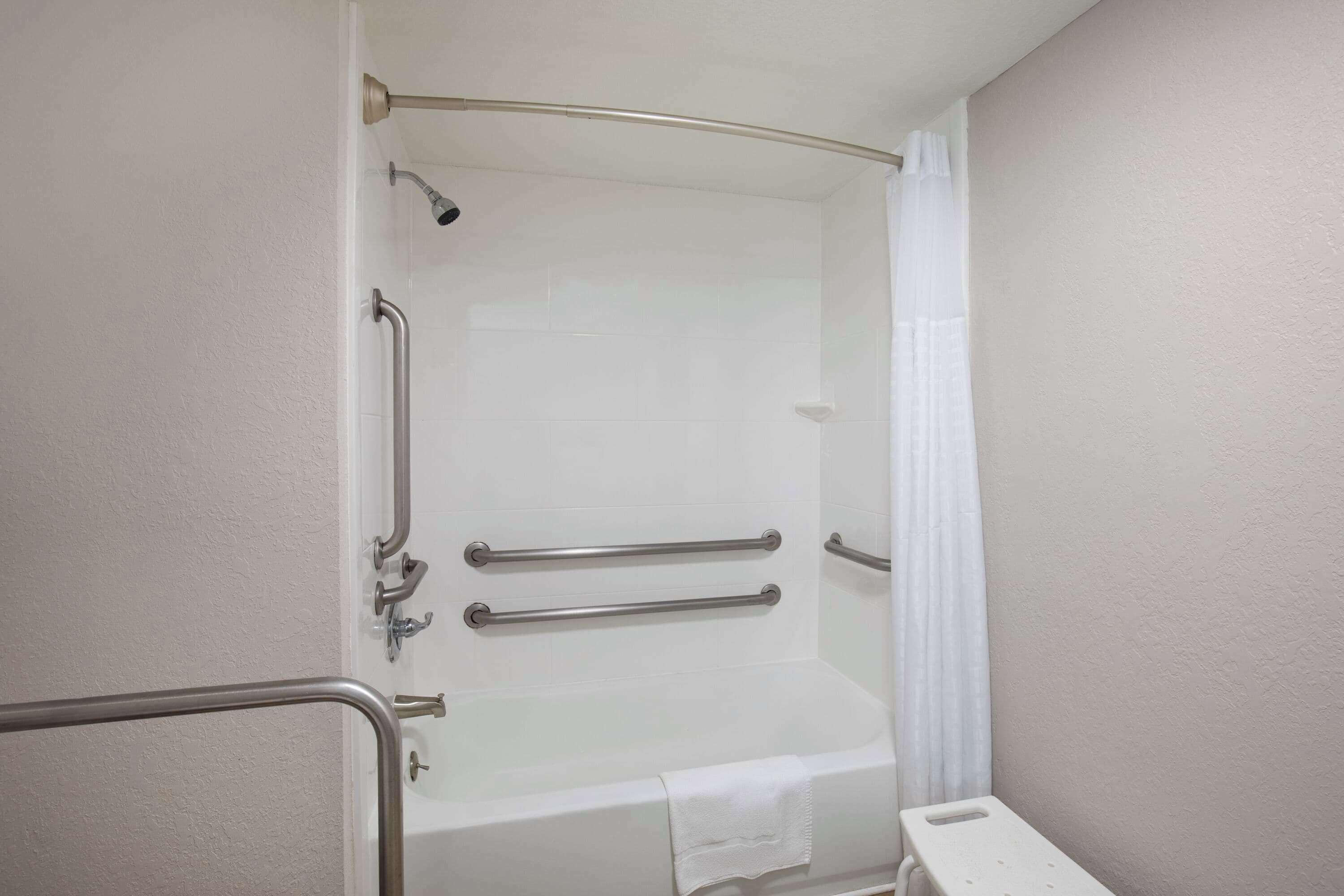 A bathroom with a bathtub, grab bars, and a shower curtain.