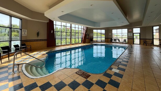 Una piscina interior con suelo a cuadros, una escalera de piscina y sillas alrededor del borde.